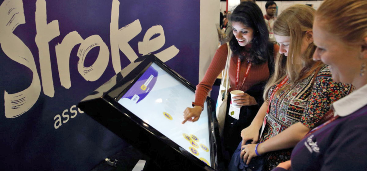 Three women interacting with a large touchscreen. 