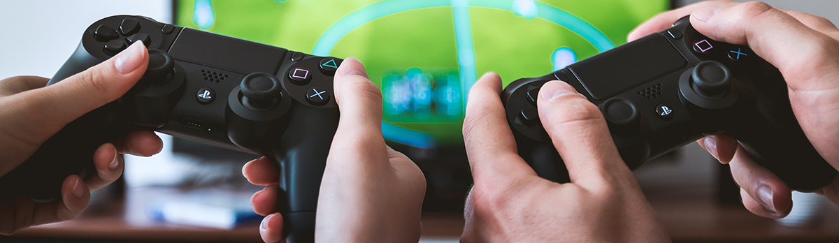 Two sets of hands holding PlayStation 4 controllers and playing a Football game.