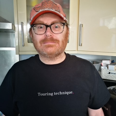 Peter Bithell in the kitchen, smiling. He's wearing a t-shirt that says: Touring technique.