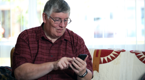 Photo of Bill, a stroke survivor, looking at his smartphone and smiling